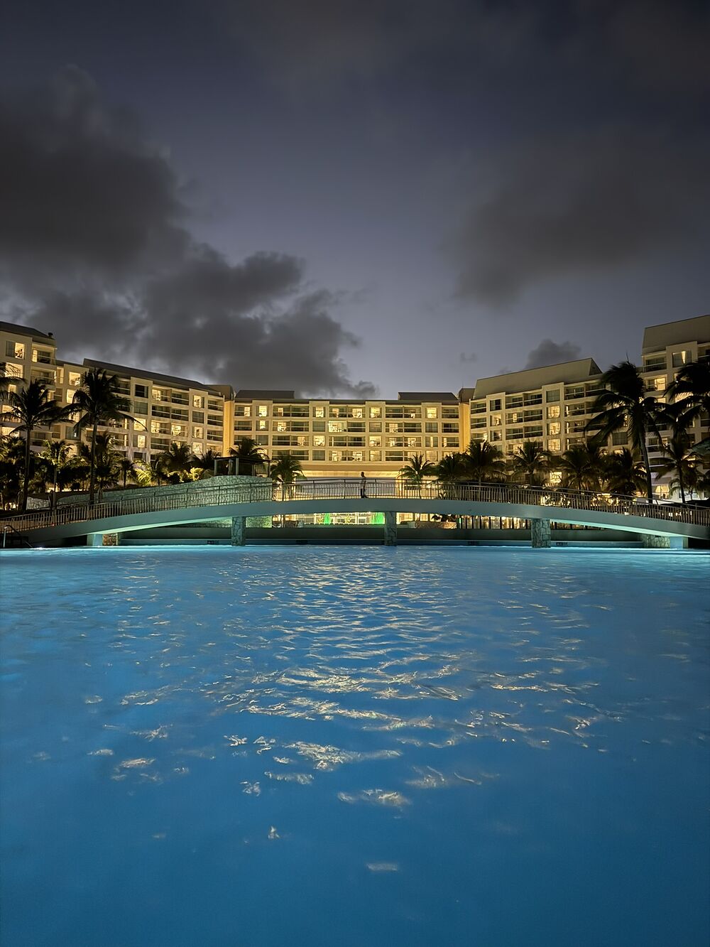 A resort pool glowing at night beneath a stormy sky