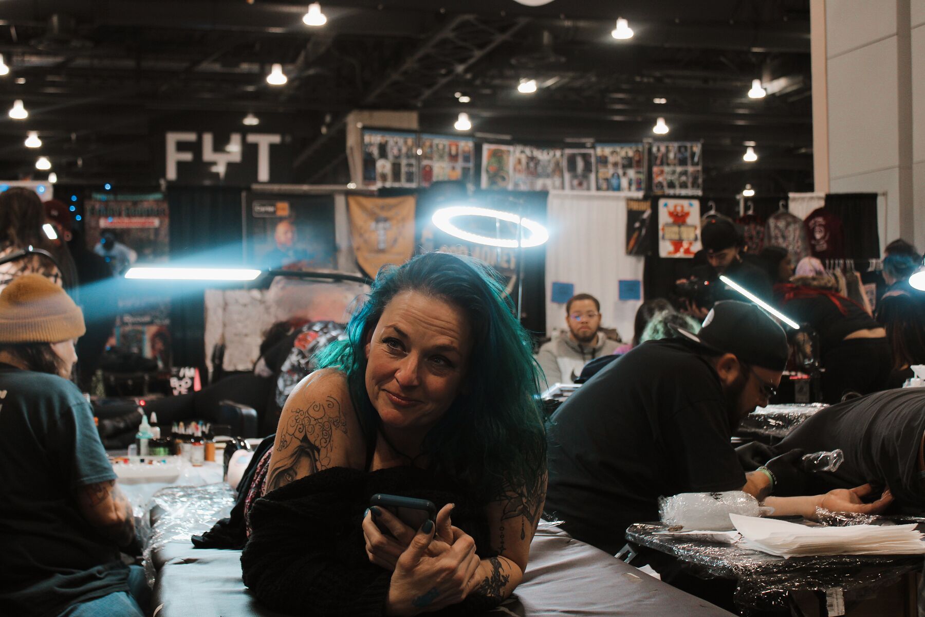 A busy tattoo convention floor with a client smiling from an artist's chair