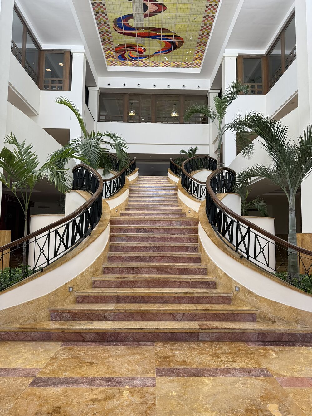 A grand hotel staircase rising between palms and white balconies